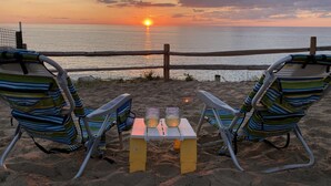 Deux chaises de plage sont placées face à un coucher de soleil sur l’océan, avec une petite table entre elles.
