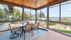 Une terrasse couverte avec une table et des chaises, de grandes fenêtres et une vue sur l’océan.