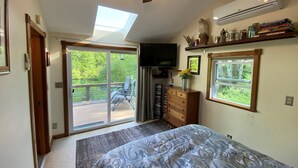 Un dormitorio con cama, ventilador de techo, televisión, estantería y ventana con vista a follaje.