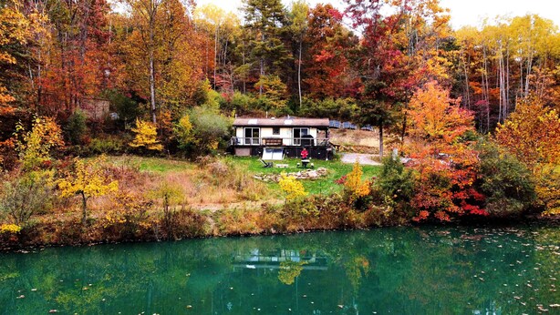 Una cabaña con terraza y paneles solares, rodeada de follaje otoñal y un lago.