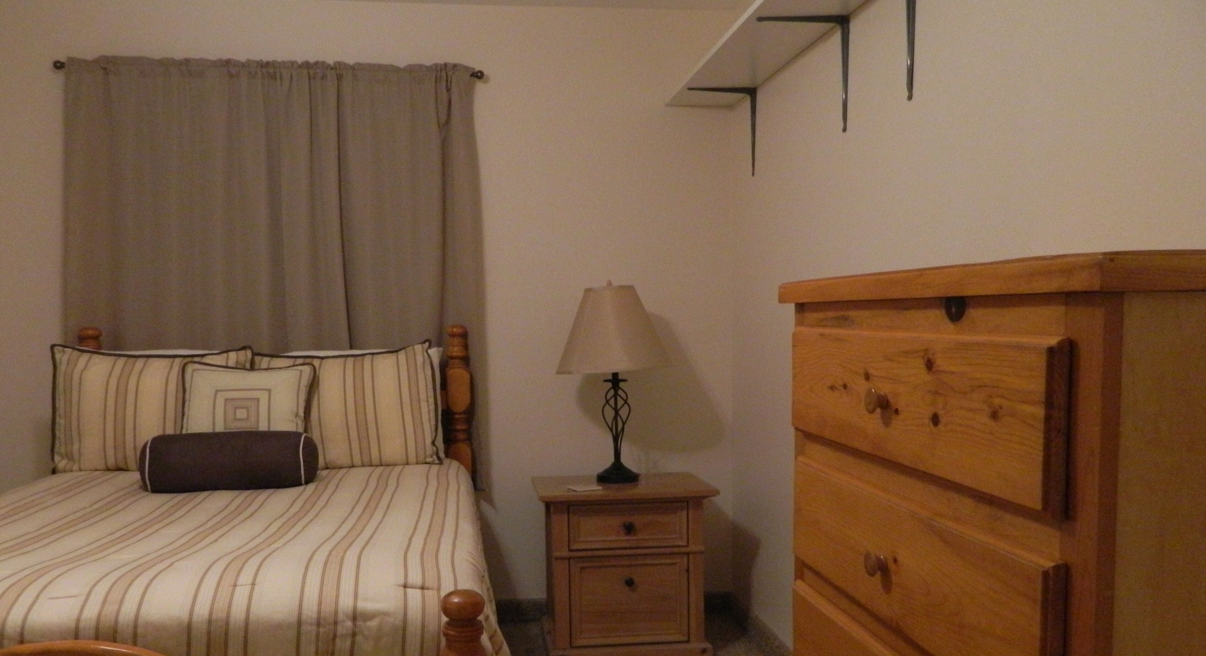 Un dormitorio con una cama, una mesita de noche, una lámpara y un aparador de madera.