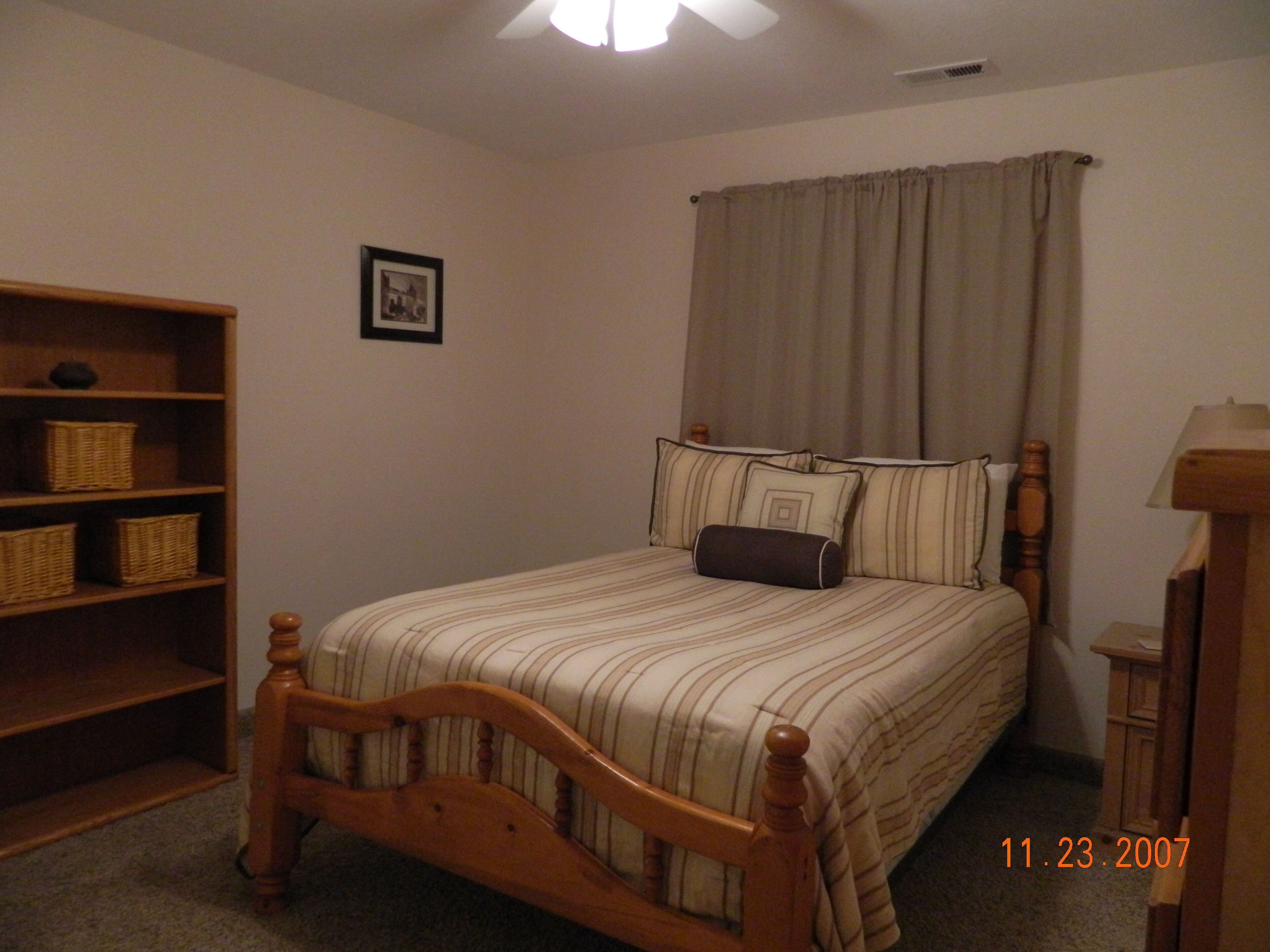 Un dormitorio con una cama de madera, una mesita de noche, una lámpara, una estantería con cestas y un cuadro en la pared.