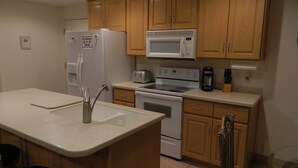 A kitchen with wooden cabinets, a refrigerator, a microwave, a toaster, and a coffee maker. - Gateway to Zion - Sleeps 8! (Hurricane)