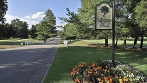 A sign for Nashboro Woods with a road leading through a park-like setting.