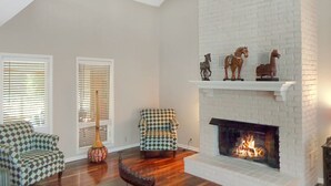 A living room with a fireplace, two patterned armchairs, a floor lamp, and decorative horse statues on the mantel.