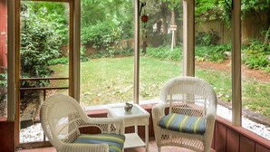 A sunroom with wicker furniture, a small table, and a view of a garden.