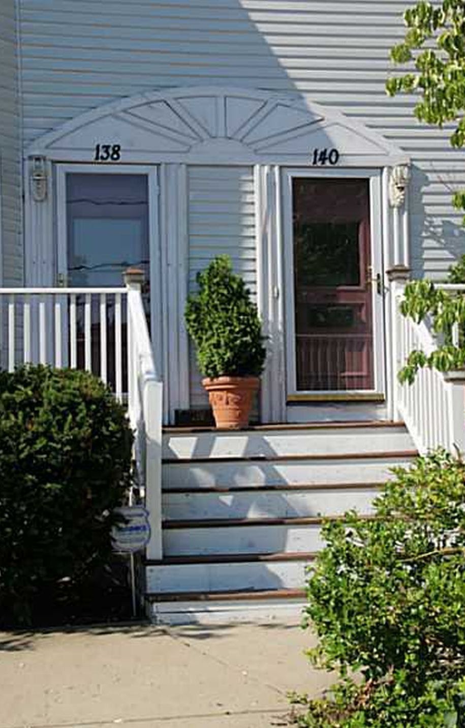 A two-story house with a front porch, numbered 138 and 140, and a potted plant on the steps.