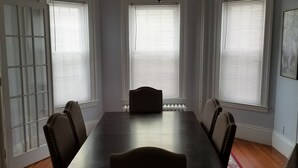 A dining room with a rectangular table, six chairs, a chandelier, and three windows with blinds. - Spacious Condo In Cranston/Providence Line - 2 Bed (Cranston)