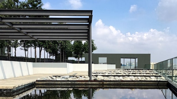 Un edificio moderno con una piscina reflectante, barandillas metálicas y un cielo despejado.