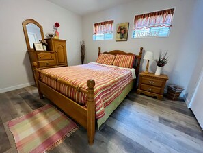 Une chambre à coucher avec un lit en bois, une table de chevet, une commode, un miroir et une fenêtre avec des rideaux.