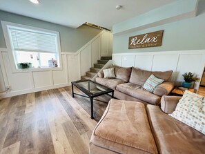 Un salon avec un canapé beige, une table basse en verre et un escalier en arrière-plan.