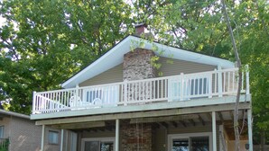 A two-story house with a balcony, stone foundation, and a gravel driveway. - 10MM Lake Getaway - 3 Br, 2 Bath - Franky & Louie's Cove! (Sunrise Beach)