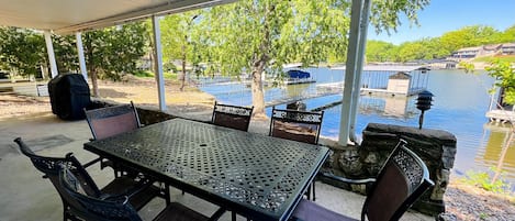 Eine Terrasse im Freien mit Tisch und Stühlen, mit Blick auf ein Gewässer und Gebäude.