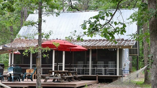 A covered outdoor seating area with picnic tables and umbrellas, surrounded by trees.