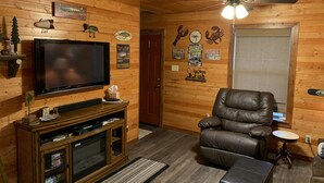 A cozy cabin interior with a television, leather chair, wooden walls, and various fishing-themed decorations.