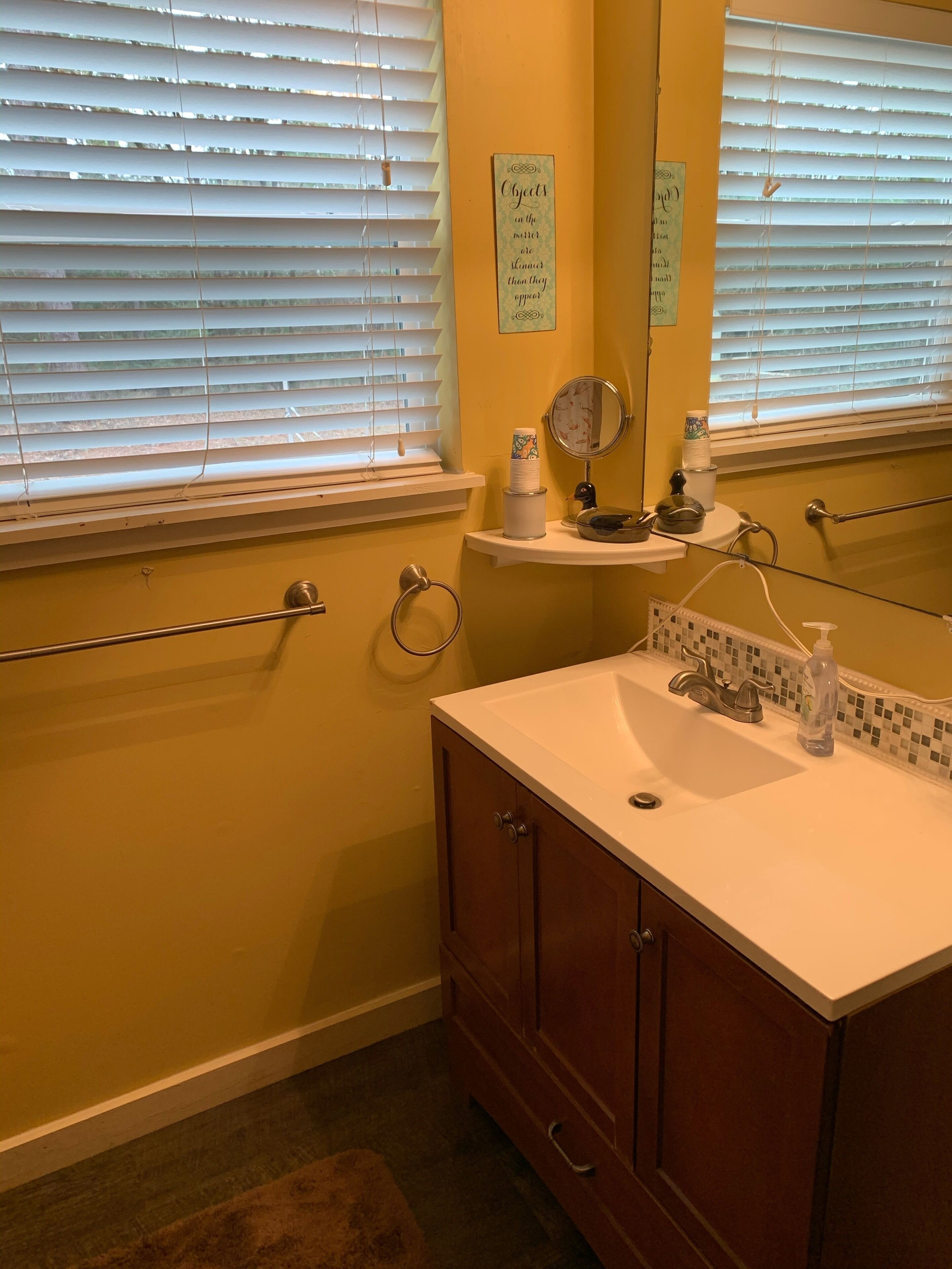 A bathroom with a white sink, wooden vanity, and a mirror above it. There are towels on a rack and a shelf with toiletries.
