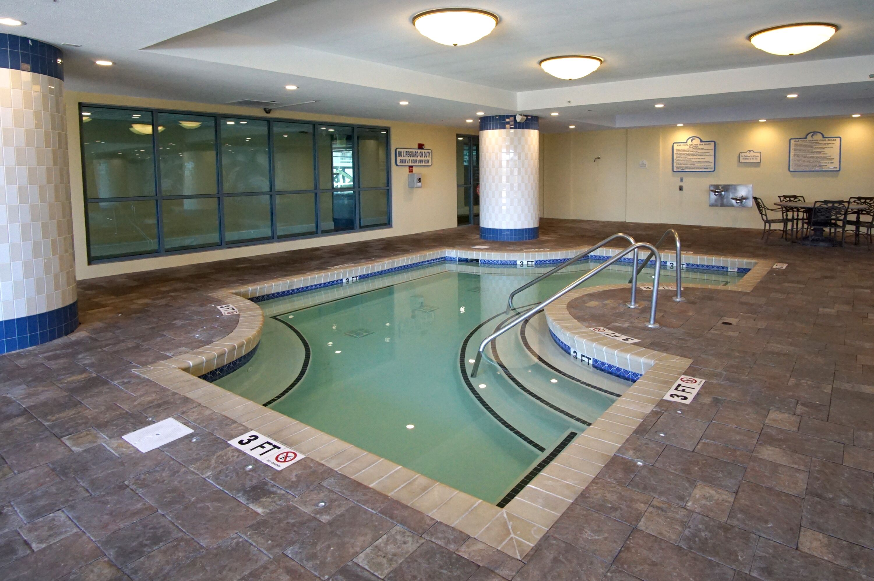 Una piscina interior con marcas de carriles visibles, una estación de socorristas y una zona de estar con paneles informativos.