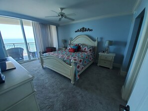 Une chambre à coucher comprenant un lit, un bureau, une chaise, une table de chevet, une lampe et un ventilateur de plafond.