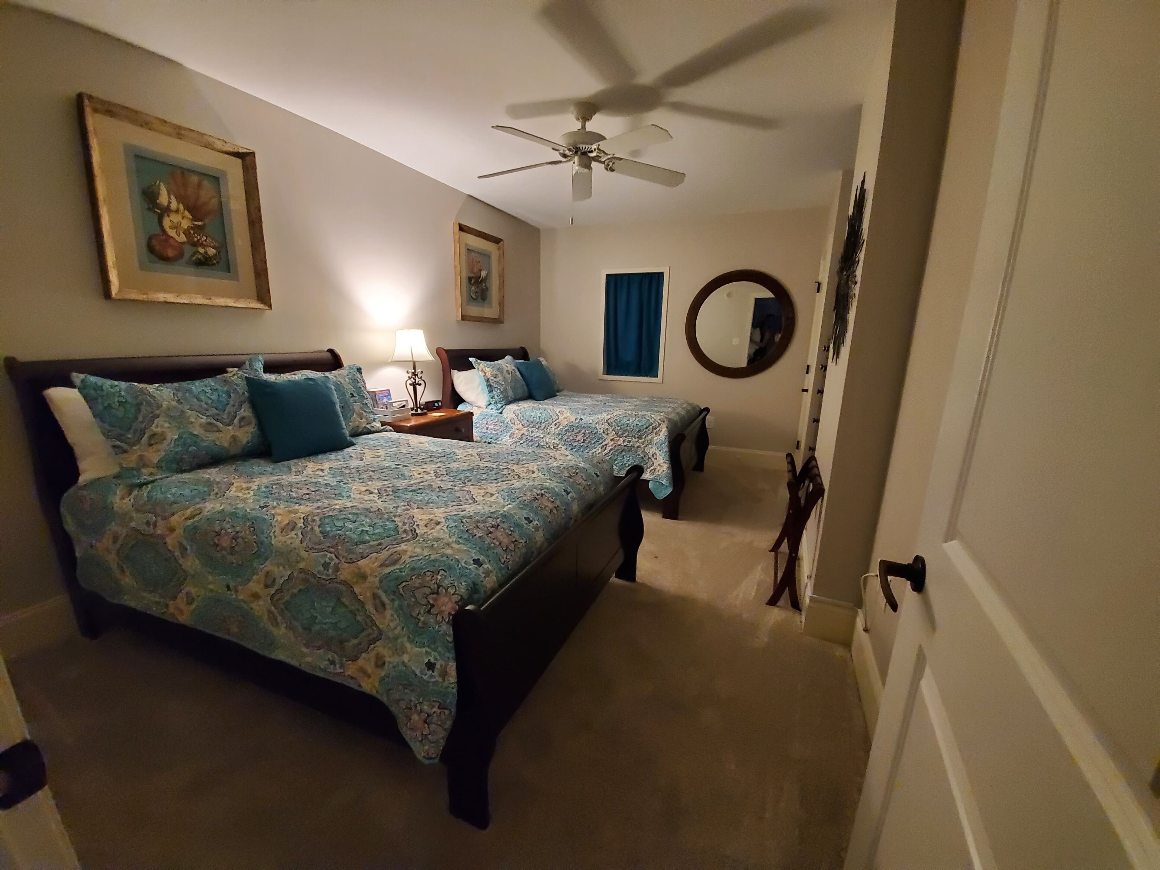 Een slaapkamer met een bed, nachtkastje, plafondventilator, een lijst met een foto en een spiegel.