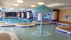 En indendørs swimmingpool med flere baner, et centralt vandelement og flisegulv.