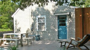 Une petite maison avec une porte bleue, une terrasse avec une table et des chaises, et une clôture en bois.