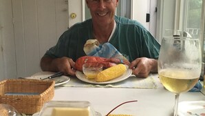 Une table à manger avec un homard, des épis de maïs et un verre de vin blanc.