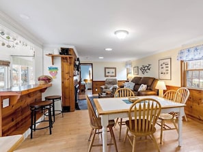 Un interior acogedor con una mesa de comedor de madera, taburetes de bar, un sofá y un televisor.