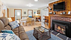 Un salon doté d’une cheminée, d’un téléviseur fixé au mur et d’un coin repas avec des meubles en bois.