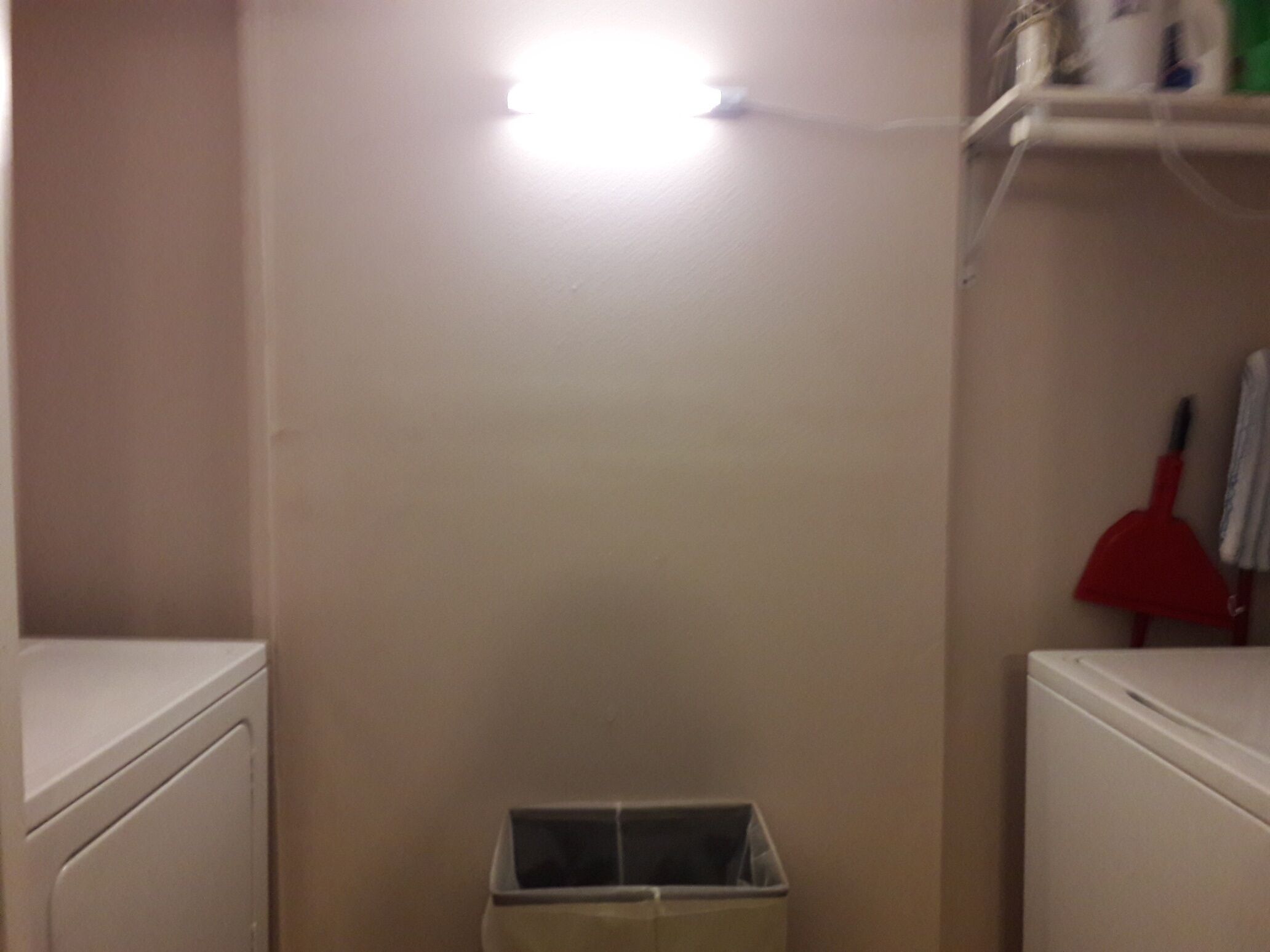 A laundry room with a white washing machine, a drying rack, and a trash bin.