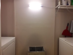 A laundry room with a white washing machine, a drying rack, and a trash bin.