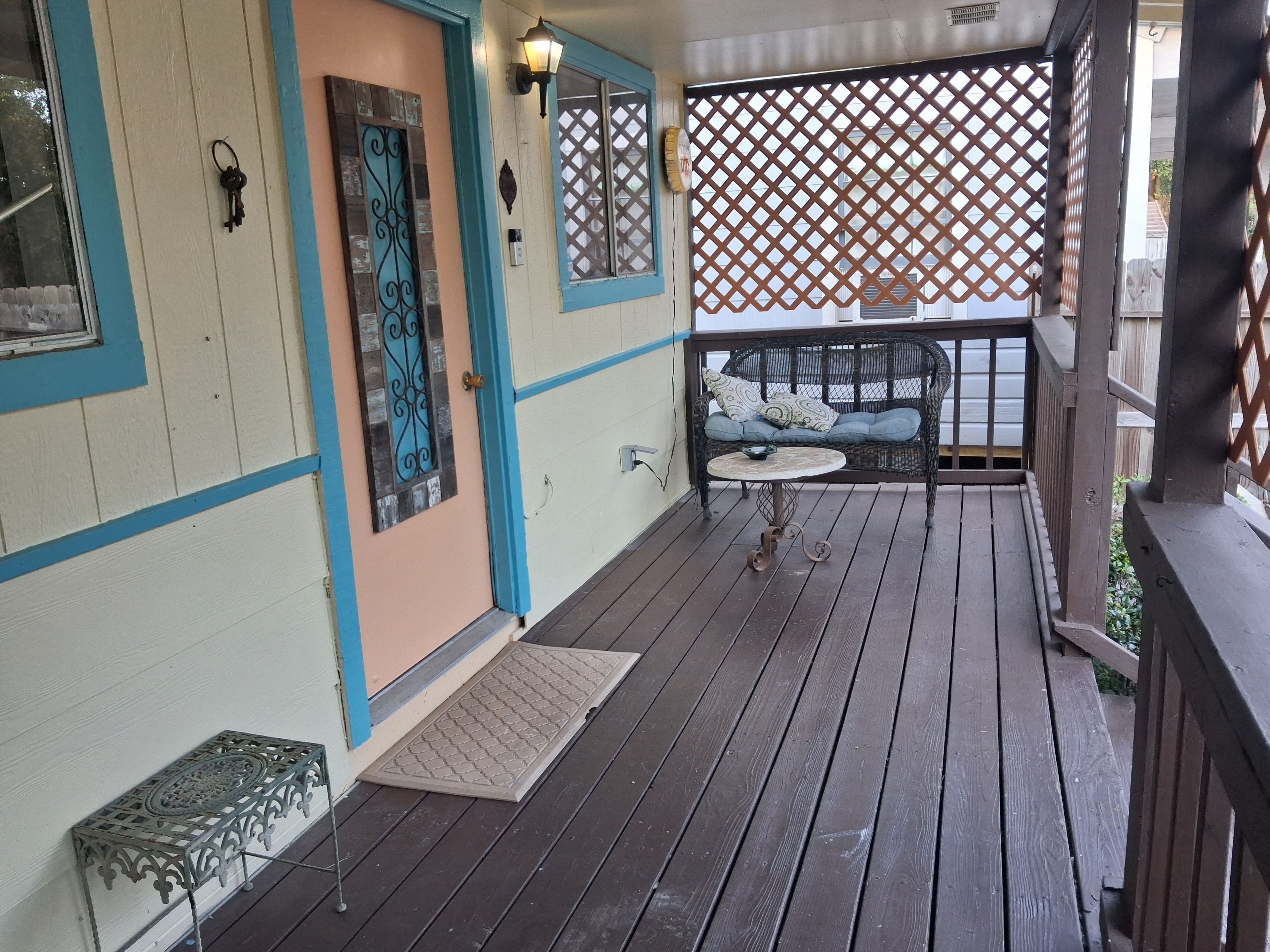 A wooden deck with a bench and a table, a door with decorative metalwork, and a lattice screen.