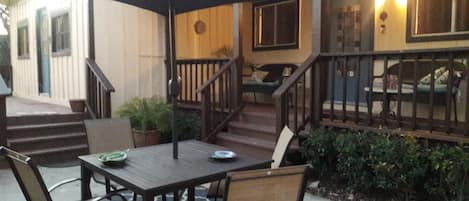 An outdoor patio with a wooden table and chairs, a large umbrella, and a staircase leading to a covered deck area.