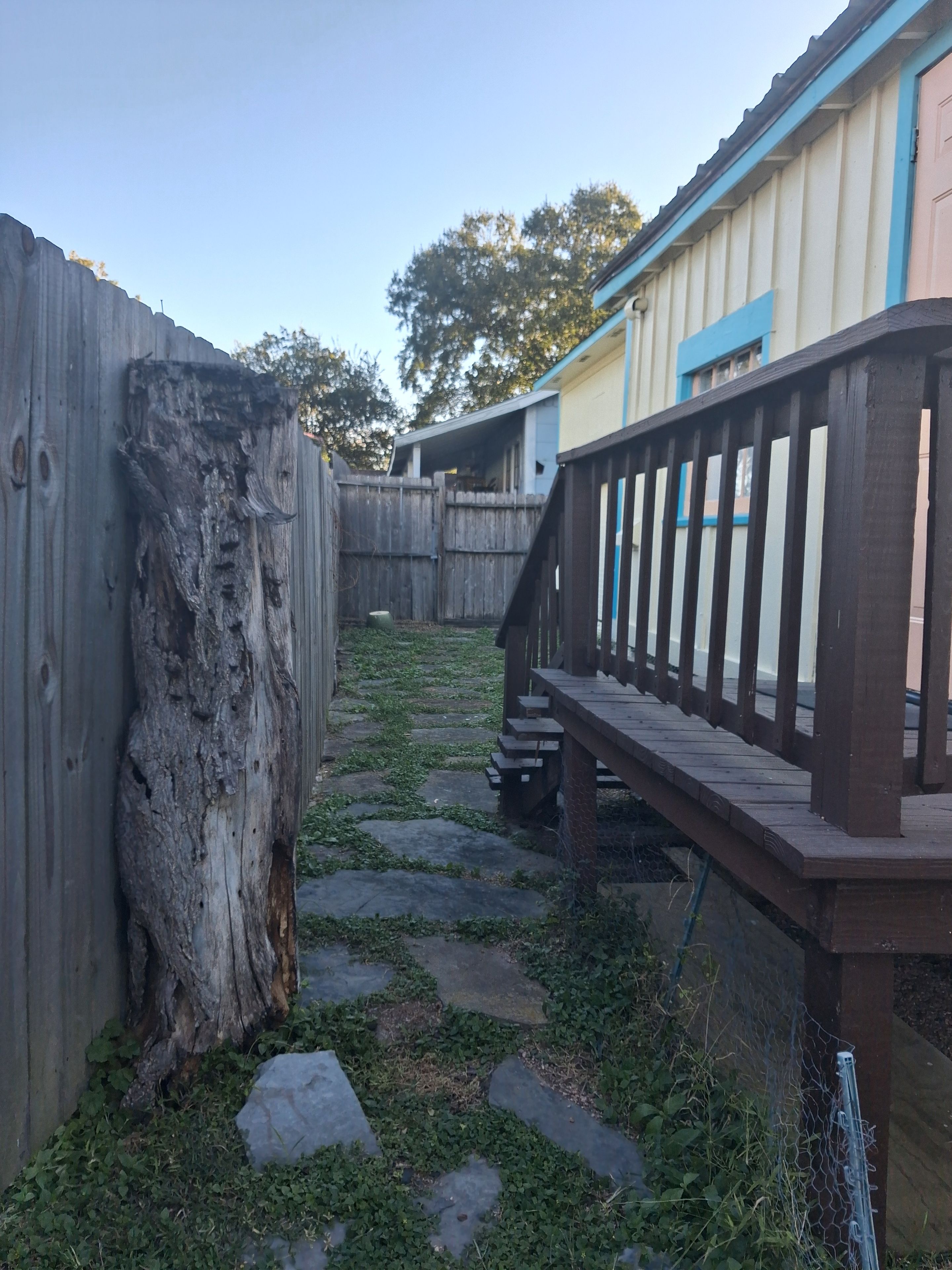 A wooden deck with a metal railing, a stone pathway, and a wooden fence.
