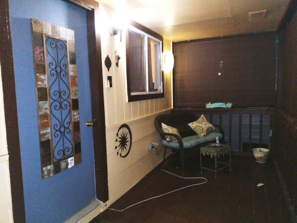 A room with a blue door, a window, a chair with cushions, a small table, and a trash bin. - Clifton By The Sea Bungalow-2 Miles from Kemah Boardwalk Dog Friendly (Bacliff)