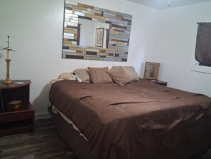 A bedroom with a bed, a nightstand, a lamp, a framed picture, and a wall art piece.