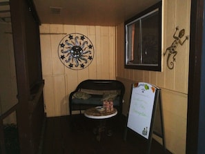 A small room with a wooden wall, a round decorative piece, a sofa, a small table with a dog figurine, and a welcome sign.
