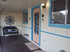 A porch with a bench, a decorative wall piece, and a door with a window.