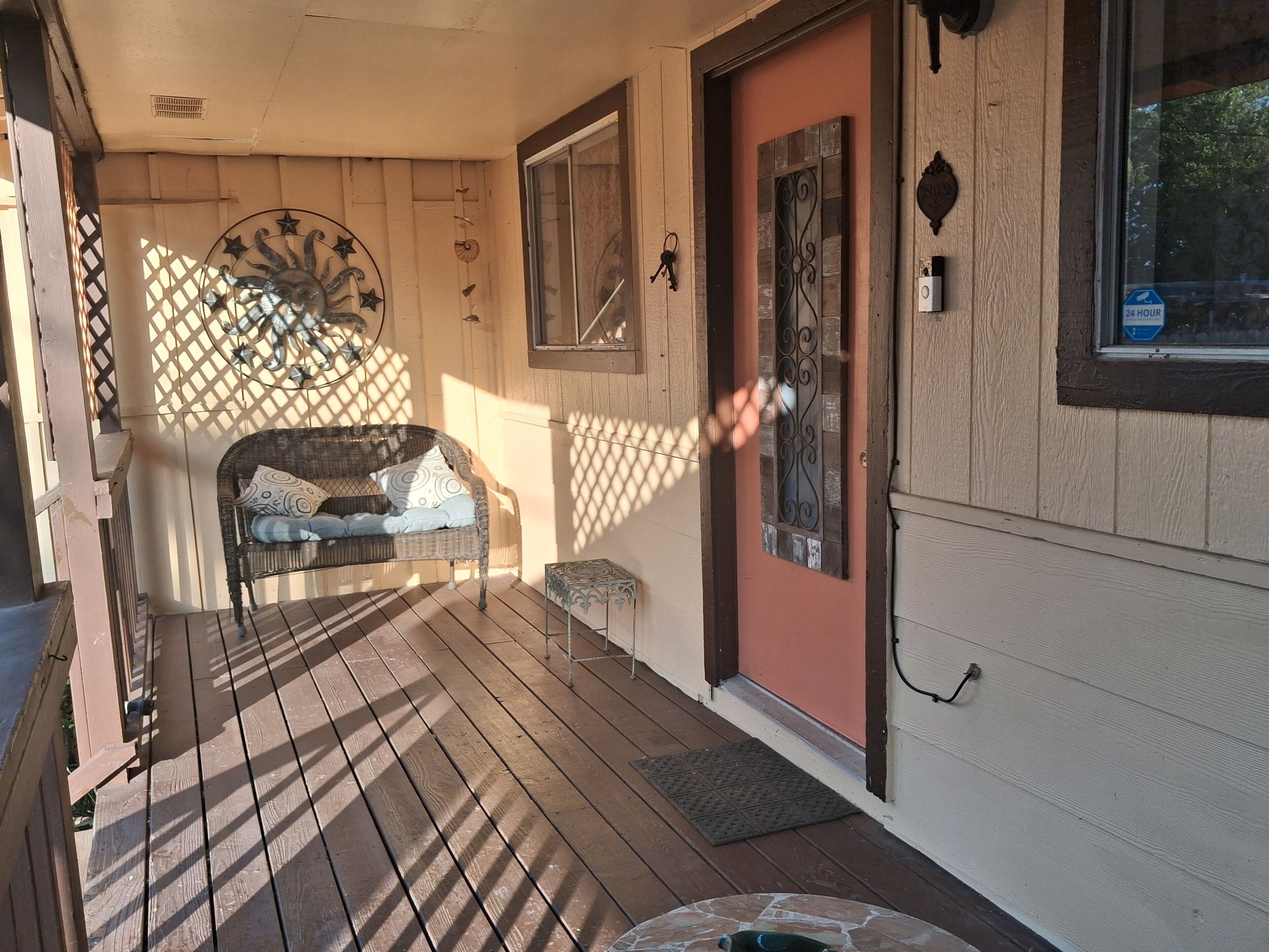 Une terrasse en bois avec un canapé en osier et une porte ornée de motifs en métal.
