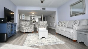Ein Wohnzimmer mit Deckenventilator, gemusterten Sesseln, einem grauen Sofa und einem blauen Schrank.
