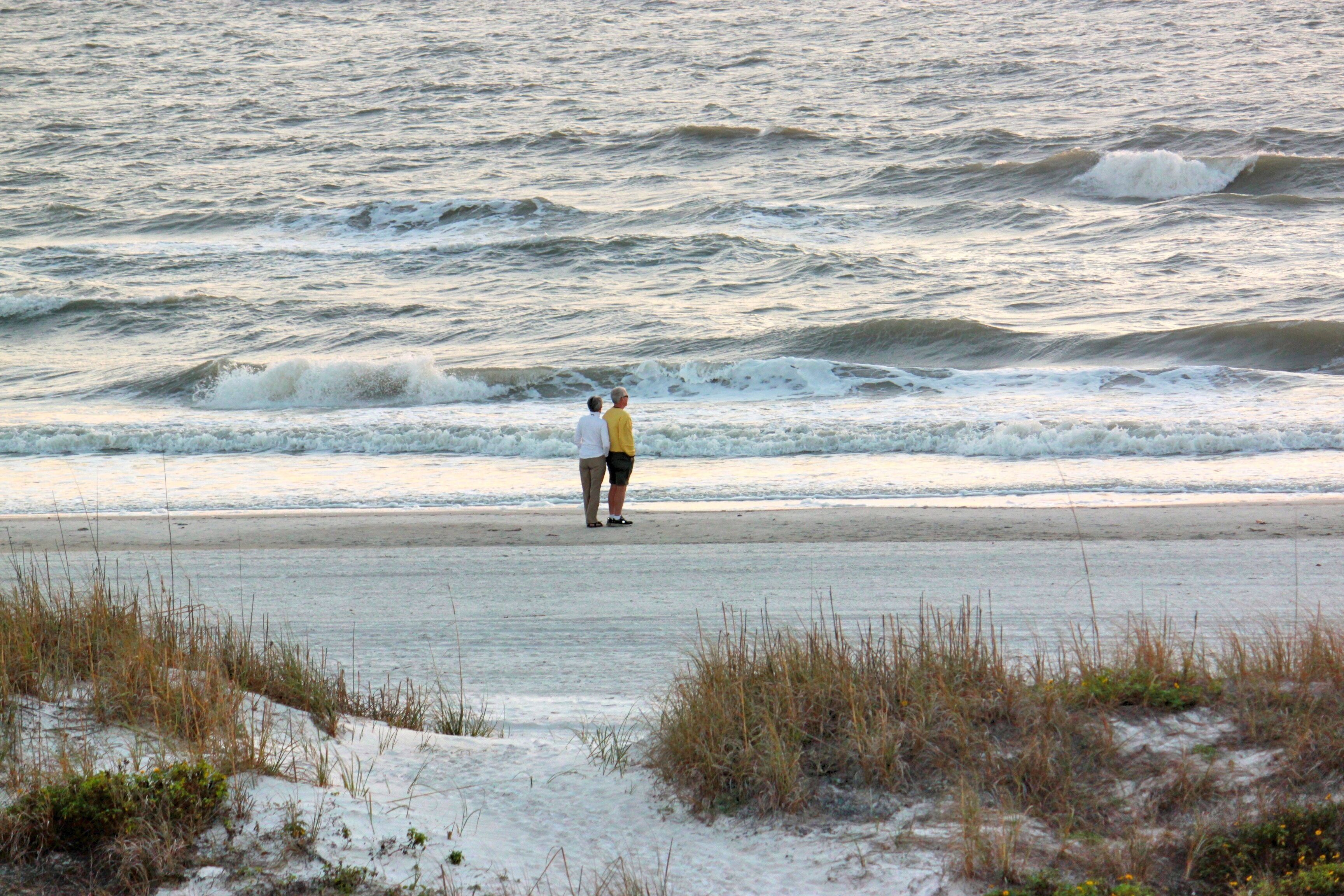 A beach with waves and a person standing on the sand.