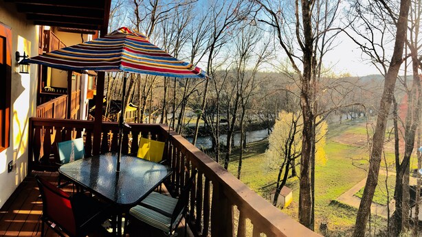 A wooden deck with a table and chairs, overlooking a river and trees.