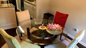 A round glass table with a central decorative piece, surrounded by four chairs with different fabric colors.