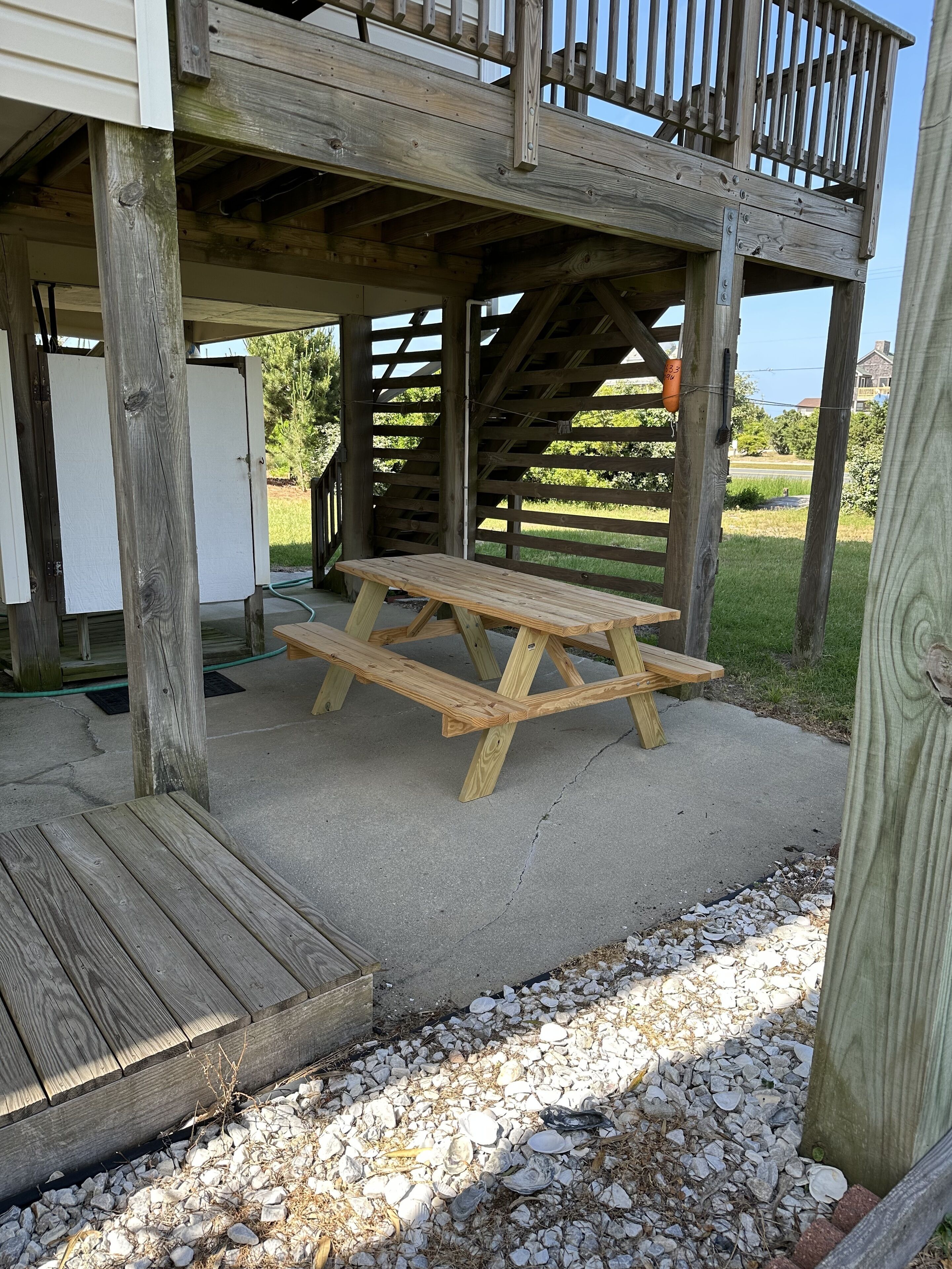 Une terrasse en bois avec une table de pique-nique, un espace couvert doté d’une rambarde et une vue sur un quartier résidentiel en arrière-plan.