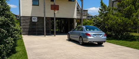 A two-story building with a basketball hoop in front, a car parked in the driveway, and a clear blue sky.