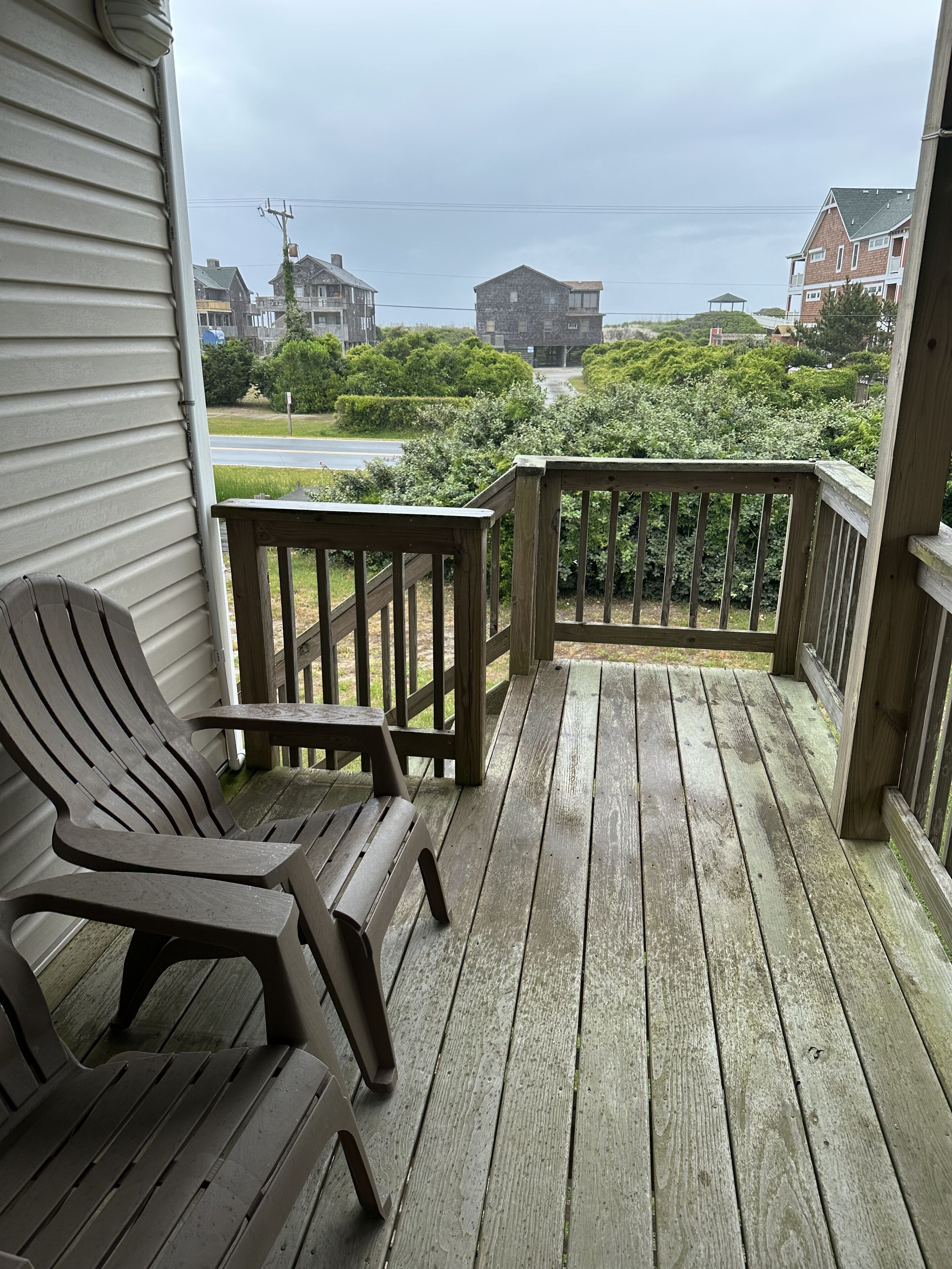 A wooden deck with a bench, overlooking a residential area with houses and a road.