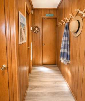 Un couloir en bois, avec une porte sur laquelle on peut lire « Maison de plage », un tableau encadré, une étoile de mer en guise de décoration et un chapeau de paille accroché au mur.