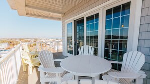 A covered outdoor patio with a round table and white Adirondack chairs, overlooking a cityscape. - Sandbridge Beach,Virginia Beach Penthouse Condominum (Virginia Beach)