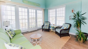 A bright living room with a green sofa, wicker chairs, a small table, and a large window. - Sandbridge Beach,Virginia Beach Penthouse Condominum (Virginia Beach)