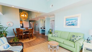 A living room with a green sofa, wicker chairs, a wooden coffee table, and a dining area with a table and chairs. - Sandbridge Beach,Virginia Beach Penthouse Condominum (Virginia Beach)