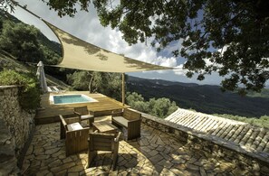 Una terraza de madera con piscina, suelo de piedra y mobiliario exterior.